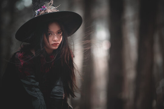 Mysterious Woman Wearing Black Witch Hat in Dark Forest Halloween Themes.