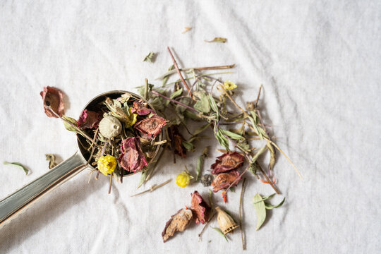Close up of a spoonful of herbal tea on a natural linen tablecloth, rustic ingredient still life and organic wellness concept