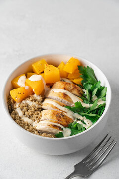 Autumn quinoa bowl with roasted pumpkin, chicken breast and fresh parsley in a bowl on a light background, healthy homemade seasonal meal