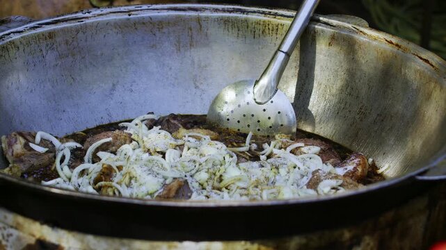 Chef Seasoning Meat and Onions in Hot Oil in Large Cauldron for Uzbek Plov