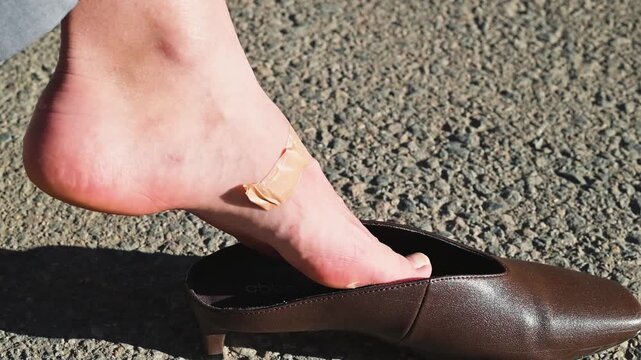 Close-up of a female foot with a callus and medical plaster in brown shoes on the street