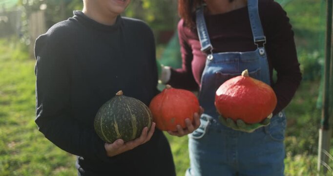 Mother and son holding organic pumpkins at vegetable home garden - Family people having fun during autumn season - Fall lifestyle concept - UGC wide lens content