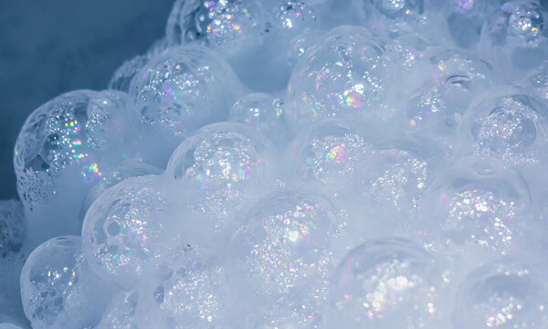 Close-up of iridescent soap bubbles and white foam on a blue studio background. Foam macro, iridescent highlights, abstract texture. Background with copy space