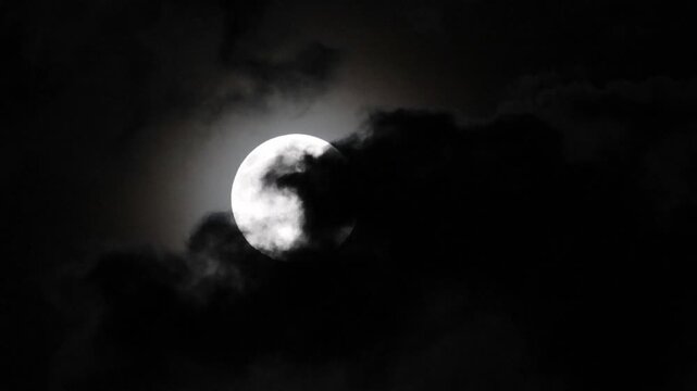The full moon illuminates the night sky, and black clouds drift across its surface
