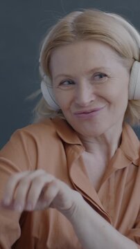 Portrait of mature lady listening to music with headphones dancing on black background. Modern technology and entertainment concept.