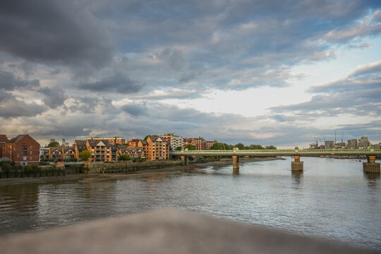Scenic view across the River Thames near Putney, London, with riverside residential buildings beneath a dramatic cloudy evening sky.