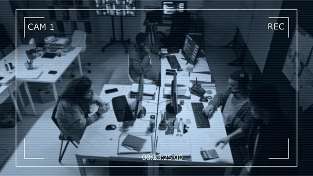 Diverse young adult programmers working late in open office captured by CCTV camera. Footage fits corporate cybersecurity, data protection, workplace surveillance advertising