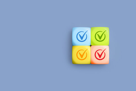 Four colorful cubes with checkmark icons in circle on blue background with copy space. Quality control, checklist completion, task management, compliance and business approval concept.