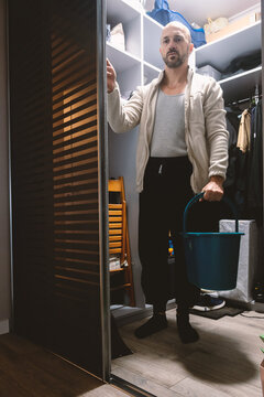 A mature man standing in a walk-in closet holding a bucket of water during home chores