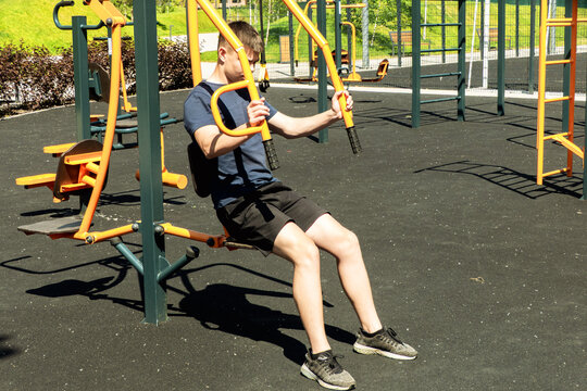 Young man working out on modern outdoor fitness equipment at public gym park