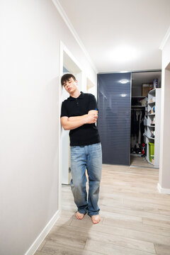 Sad teenage boy leaning against the wall in a hallway with eyes closed feeling tired or stressed