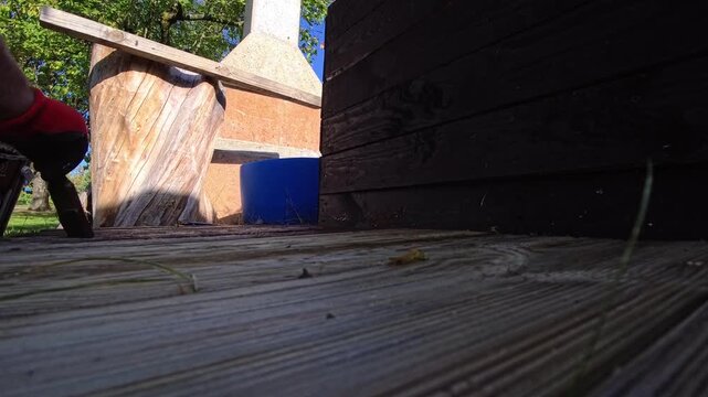 Applying Dark Wood Stain to Deck Boards in Summer Garden