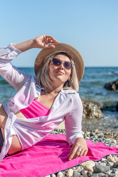 Vacation leisure portrait of blonde woman lying on pebble beach wearing hat and sunglasses