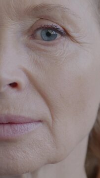 Close-up portrait of mature lady half face looking at camera with no emotion on gray background. Senior person and face expression concept.