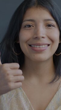 Portrait of glad Hispanic woman showing thumbs-up hand gesture smiling on black background. Happy people and positive emotion concept.