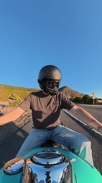 Vertical rear-facing action camera view from the motorcycle handlebar as a biker starts a turquoise custom motorcycle at sunset, with natural engine and environmental sounds.