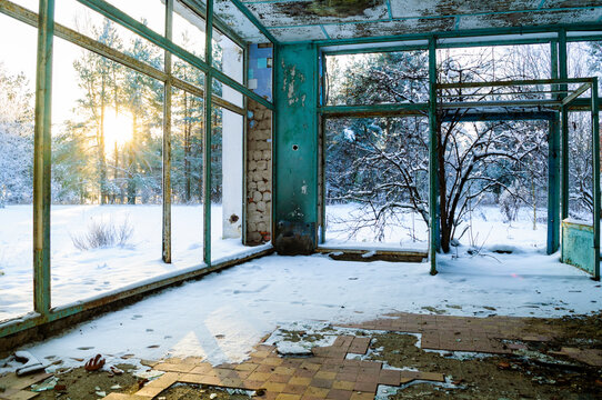 Abandoned interior background. An empty room with broken windows and snow on the floor. Rusty metal frames, peeling paint and a winter forest outside
