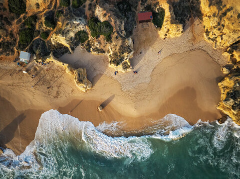 Drone top down view of Praia de Sao Rafael beach with a sandy cove, white surf, and rugged golden cliffs.