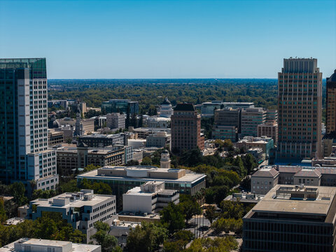 Aerial perspective across downtown Sacramento, California, showcasing office towers, tree canopies, and the distant California State Capitol dome on a clear sunny day.