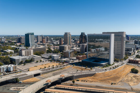 Aerial perspective of the downtown Sacramento skyline in California, showing modern high rise buildings, roadways, and the Sacramento Valley Station train tracks under clear daytime skies.
