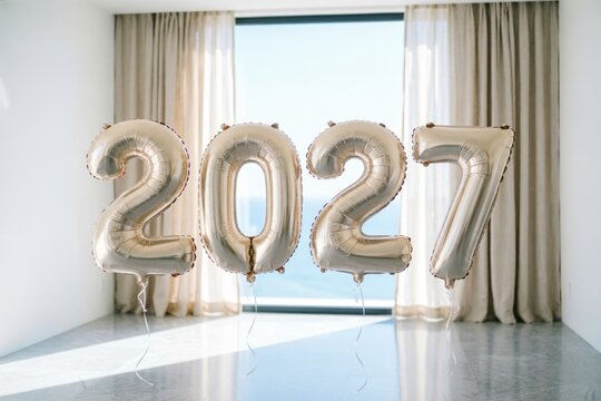 Globos plateados que forman la cifra 2027 flotan en una habitaci&oacute;n luminosa, decorada con detalles minimalistas en blanco y dorado, simbolizando la celebraci&oacute;n y el impulso hacia el futuro