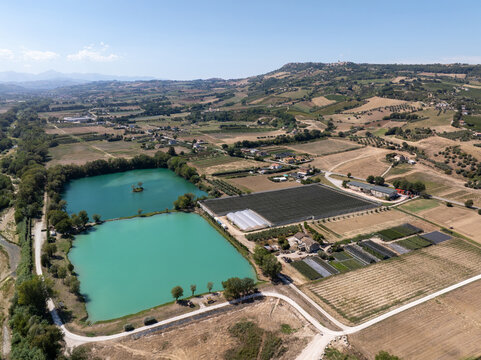 Aerial view of Laghi Santarelli with turquoise lakes, agricultural fields, and greenhouses set in the rolling hills of Moresco, Marche, Italy.