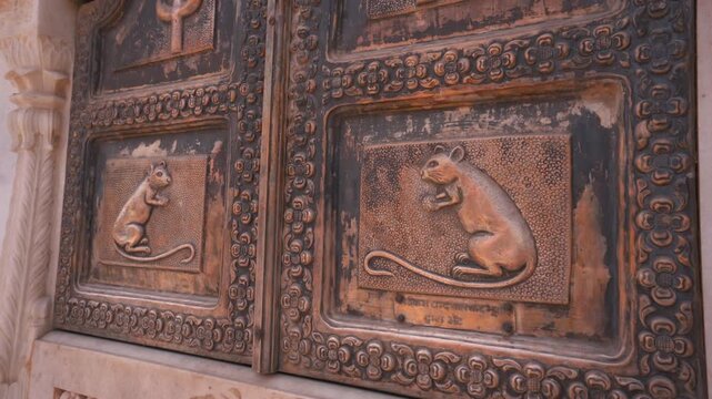 Cinematic medium close-up static shot of a carved bronze door panel featuring embossed sacred rat motifs and ornamental patterns at Karni Mata Temple in Rajasthan, India.