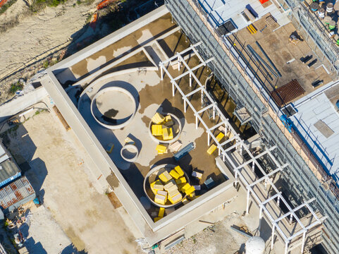 Aerial view of an Hospital construction site featuring circular structures and yellow insulation materials on a flat roof with scaffolding in Ancona, Marche, Italy.