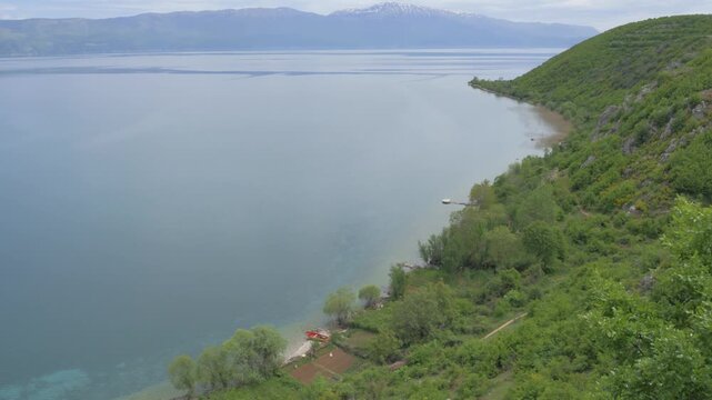 Discover the serene beauty of Lake Ohrid's expansive waters and lush green shores near Lin, Albania. Tilt up shot