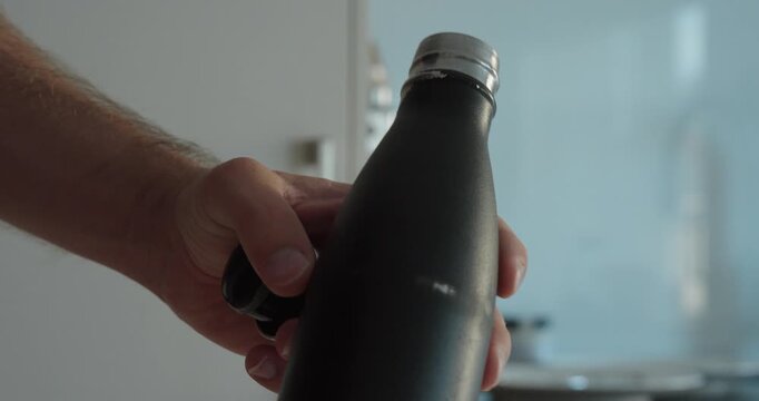Close-up of a hand pointing at chipped and peeling paint on a metal thermos bottle, showing surface wear and damage.