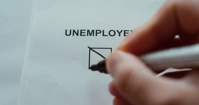 Close-up of a hand marking the unemployed checkbox on a paper form, representing unemployment and job status.