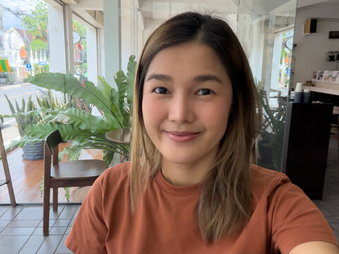 Smiling young Thai woman taking a selfie inside a modern cafe with natural light