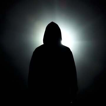 Mysterious hooded figure silhouette standing against glowing bright light in darkness.