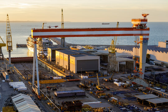 Aerial view of Ancona Port featuring a large gantry crane, industrial shipyard facilities, and a cruise ship docked at the pier during golden hour in Ancona, Marche, Italy.