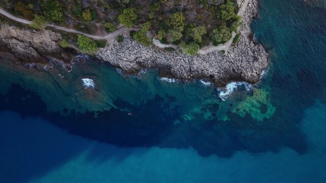 Aerial view of rocky coastline and clear blue sea with coastal path in Monaco