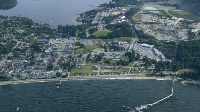 Seaside Town, Pier, Beach Shoreline, And Nearby Quarry Along The Coast In Canada. - aerial shot