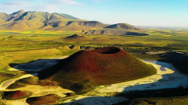 An ancient volcanic cinder cone rises from flat salt flats and yellow agricultural fields.