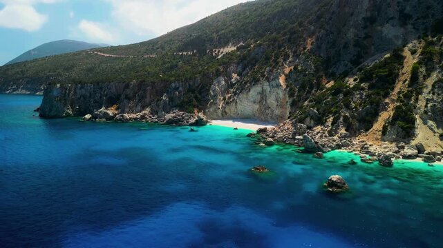 Waves break along a secluded Mediterranean shore beneath steep rocky mountain terrain.