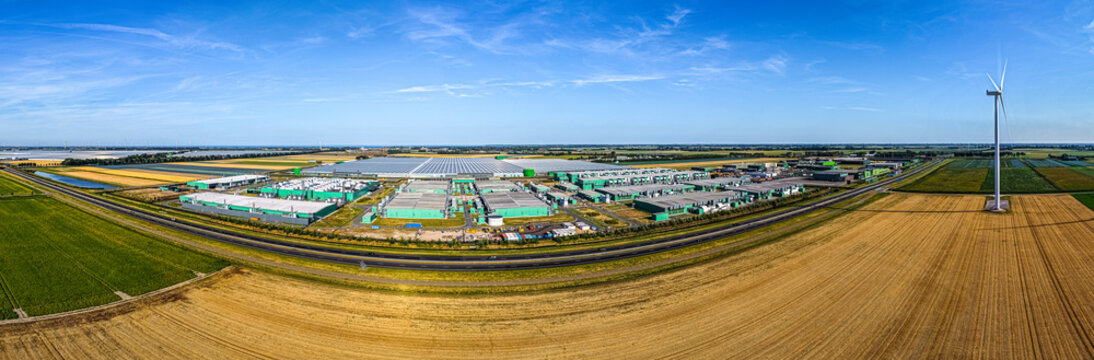 Aerial view of Agriport A7 industrial and greenhouse complex surrounded by agricultural fields and a wind turbine in Middenmeer, Noord-Holland, Netherlands.