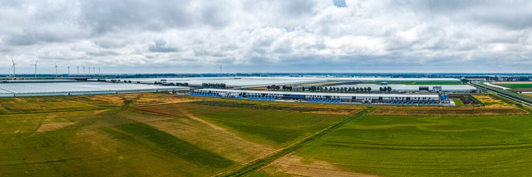 Aerial view of Agriport A7 greenhouse complex surrounded by agricultural fields and wind turbines under a cloudy sky in Middenmeer, Noord-Holland, Netherlands.