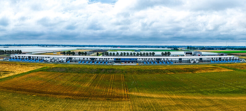 Aerial view of Agriport A7, a large industrial greenhouse complex surrounded by expansive agricultural fields under a cloudy sky in Middenmeer, Noord-Holland, Netherlands.