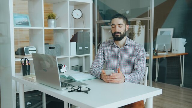 Good-looking Middle Eastern business man is touching smartphone screen working at table in office sitting alone. People and communication concept.