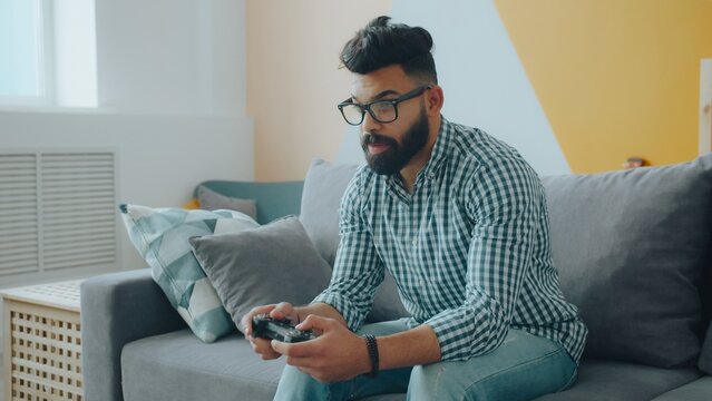 young mixed race man enjoying video game relaxing on couch in cozy apartment playing alone. People, housing and hobby concept.