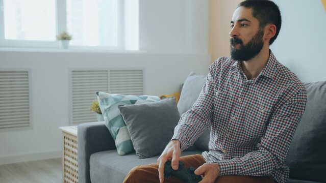 good-looking mixed race guy enjoying video game in apartment relaxing on couch and having fun alone. People and hobbies concept.