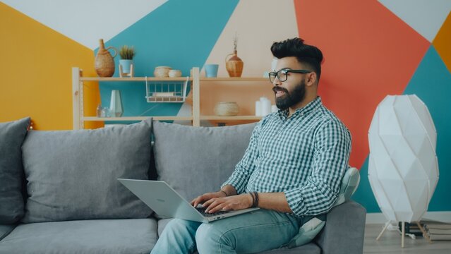 Good-looking Arab man freelancer is using laptop working from apartment alone concentrated on remote work. People and freelance job concept.