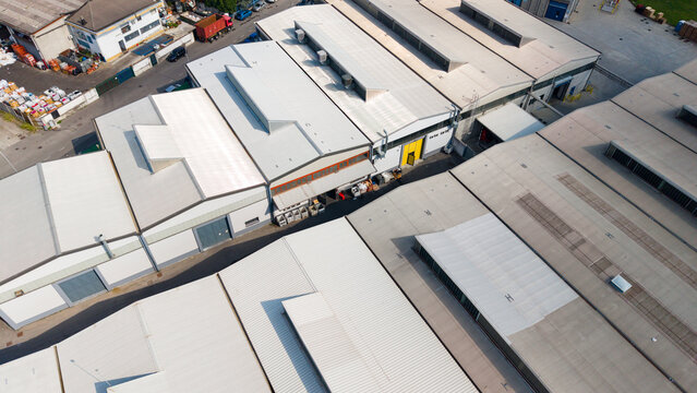 Aerial view of warehouse roofs in an industrial zone with metal structures and skylights in Milan, Lombardy, Italy.