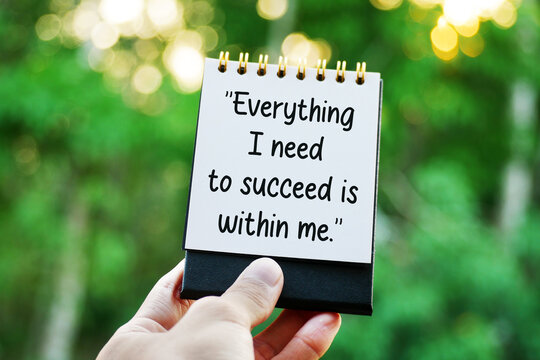 Hand holding notepad with Everything I need to succeed is within me text in green forest