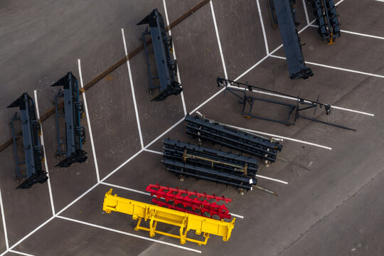 Aerial view of agricultural harvesting machinery components, including headers and augers, arranged in a parking lot at a manufacturing facility in Plock, Masovian Voivodeship, Poland.