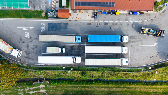 Aerial view of a truck parking area with several semi-trucks parked in marked bays at a rest stop in Milan, Lombardy, Italy.