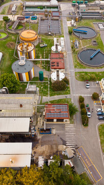 Aerial view of the Depuratore di San Giuliano Milanese Ovest wastewater treatment plant with circular sedimentation tanks, industrial buildings, and access roads in Rancate, Lombardia, Italy.